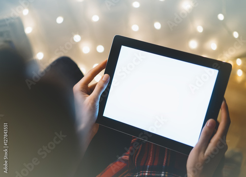 Hipster girl using tablet technology in home atmosphere, person holding computer on background glow bokeh Christmas illumination, hands texting on relax glitter xmas decoration, mockup templates