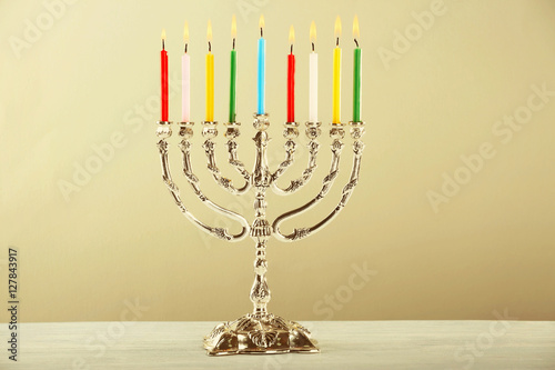 Menorah with colorful candles for Hanukkah on wooden table against light background