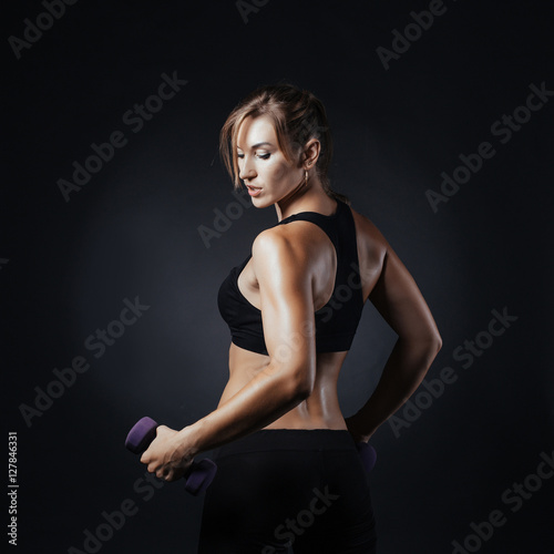 Muscular fitness woman posing on a dark background in studio