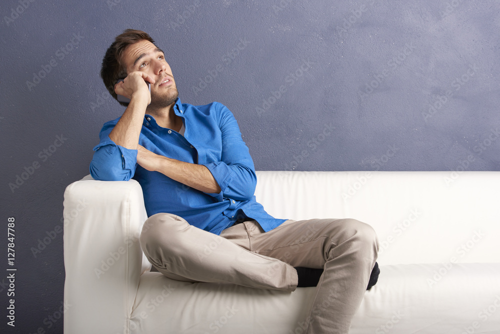 Young man with cellphone. Portrait of a thoughtful young man with mobile phone relaxing on couch and looking up. Young man with cellphone. Portrait of a thoughtful young man with mobile phone relaxing on couch and looking up.