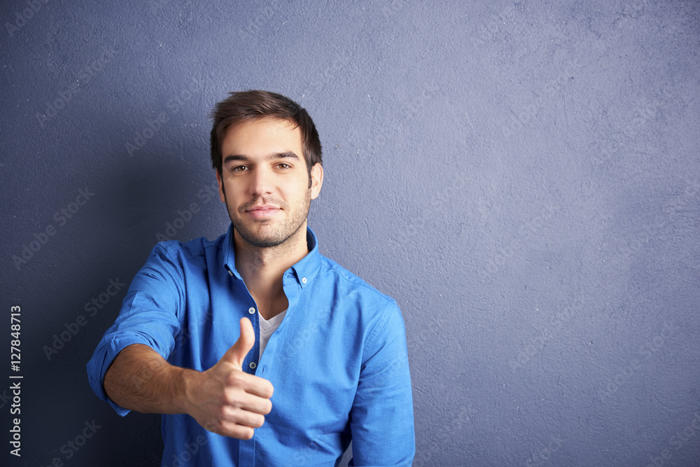 Thumbs-up. Young man standing by the wall with thumbs-up gesture. Thumbs-up. Young man standing by the wall with thumbs-up gesture.