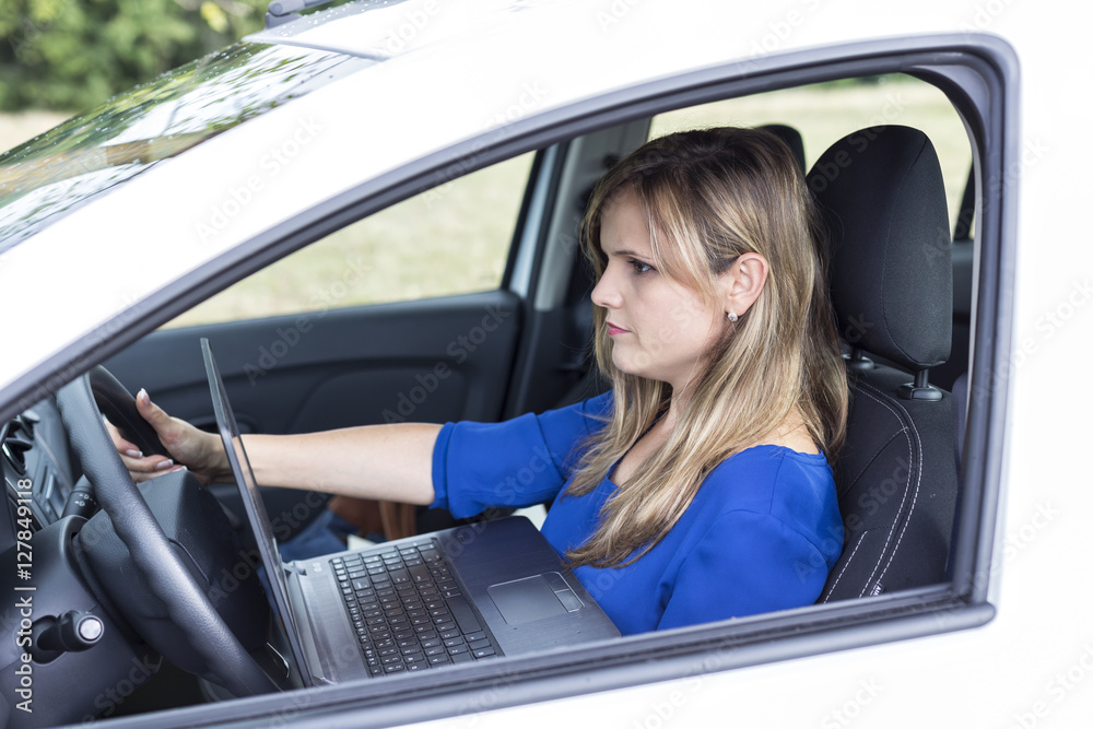 Young woman using laptop in her car while driving