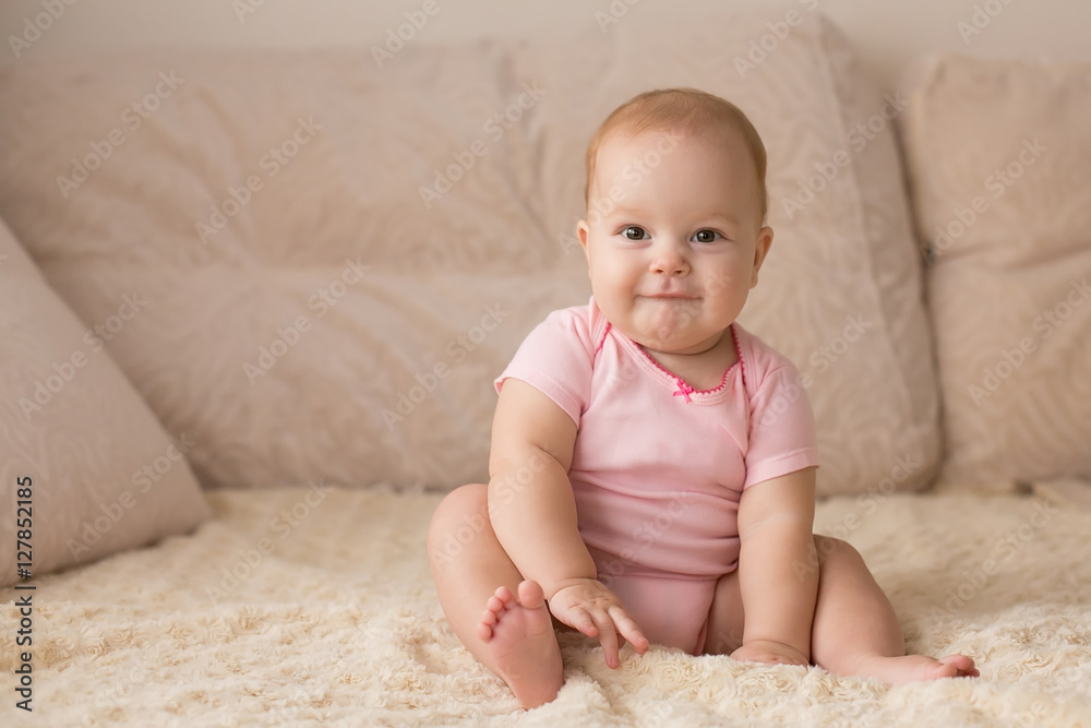 Cute smiling baby in pink bodysuit on a beige couch... Cute smiling baby in pink bodysuit on a beige couch...