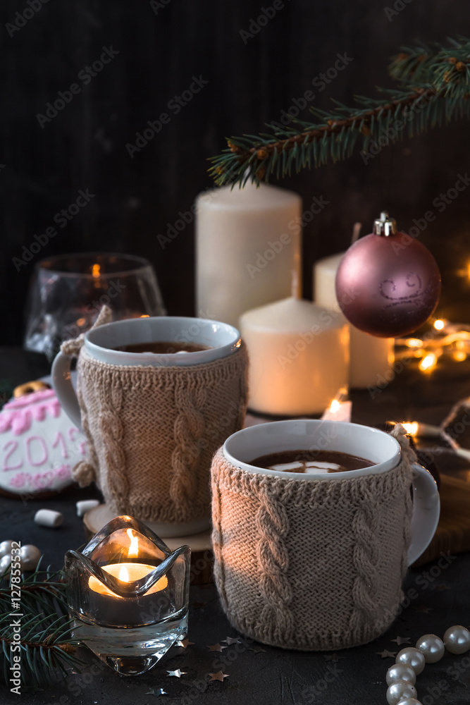 Two cups in knitted mittens of fresh hot cocoa or chocolate on wooden christmas background, dark photo