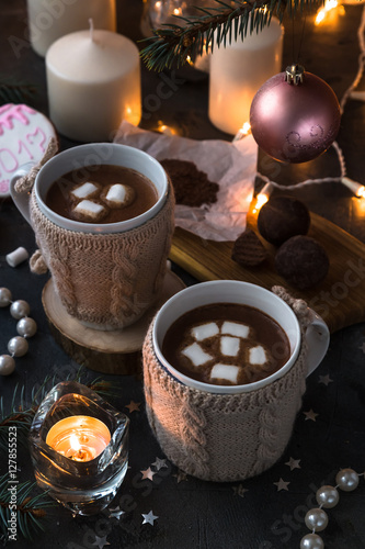 Two cups in knitted mittens of fresh hot cocoa or chocolate on wooden christmas background, dark photo