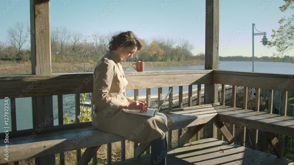 Woman sits on the lake and surfs the internet with laptop Woman sits on the lake and surfs the internet with laptop
