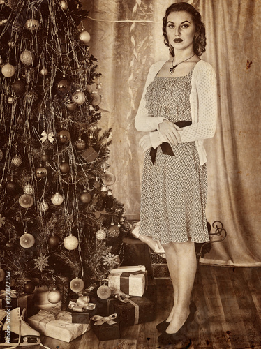 Portrait of woman receiving gifts under Christmas tree. Old photo on yellow paper. Retro style pictures. photo