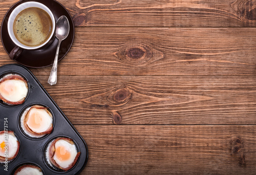 Breakfast baked eggs with bacon in muffin tin. Cup of coffe.