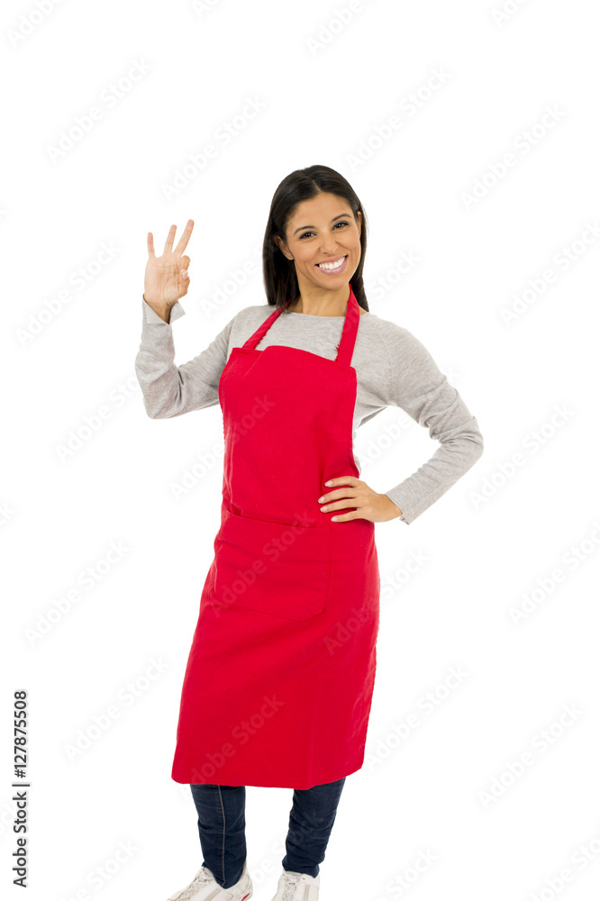 corporate portrait of young attractive hispanic home cook woman in red apron posing happy and smiling isolated
