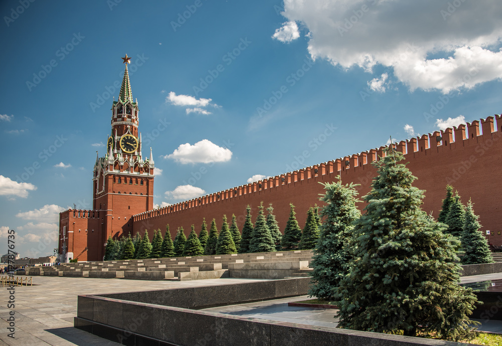 Red Square Moscow - Russia. Sunny day at the Red Square with blue sky, white clouds, green fir-trees, the Spasskaya Tower with the Kremlin chimes, the main tower with a through-passage