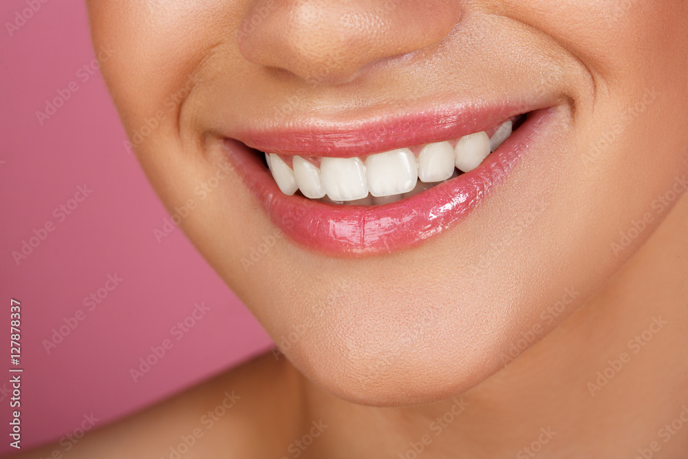 Obraz premium Beautiful smile with whitening teeth. Dental photo. Macro closeup of perfect female mouth, lipscare. Perfect pink lip makeup. Perfect clean skin, light fresh lip make-up. Pink background