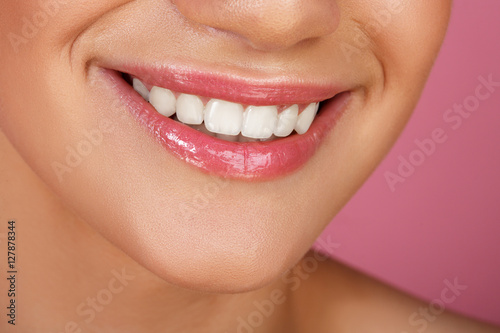 Beautiful smile with whitening teeth. Dental photo. Macro closeup of perfect female mouth  lipscare. Perfect pink lip makeup. Perfect clean skin  light fresh lip make-up. Pink background