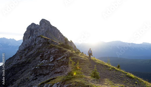 Male hiker walks along ridge of mountain during sunrise