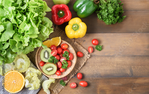 Fresh salad vegetables and fruit on wood background.