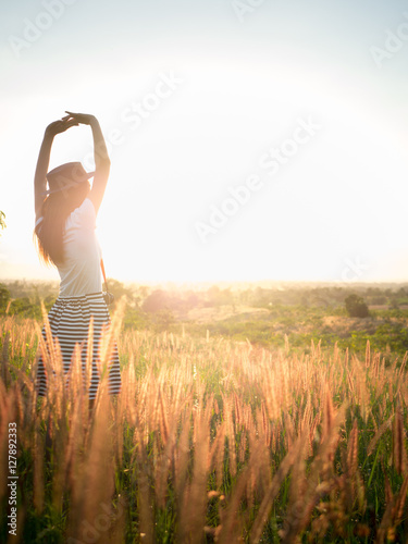 Fototapeta Naklejka Na Ścianę i Meble -  Trendy girl in stylish summer dress with beautiful hat walking in the field with flowers in sunlight