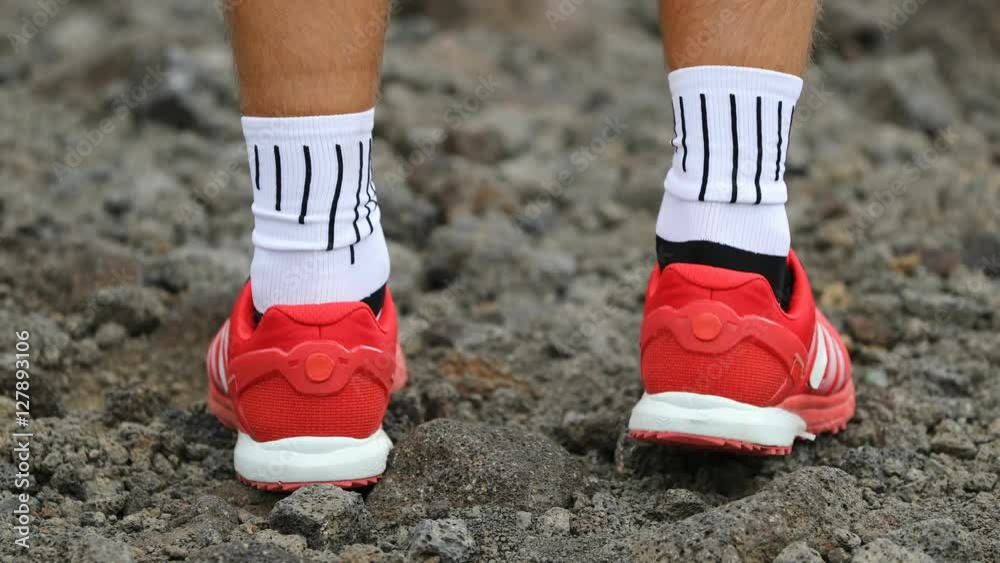 Running shoes on trail running path. Close up of male running shoes outdoors. Man wearing red shoes and white sport socks with stripes. Running shoes on trail running path. Close up of male running shoes outdoors. Man wearing red shoes and white sport socks with stripes.