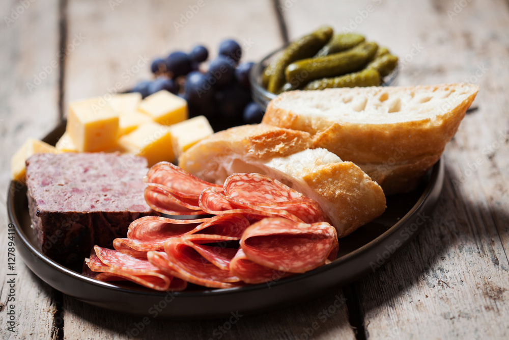 Charcuterie assortment, olives and gherkins  on plate on wooden background