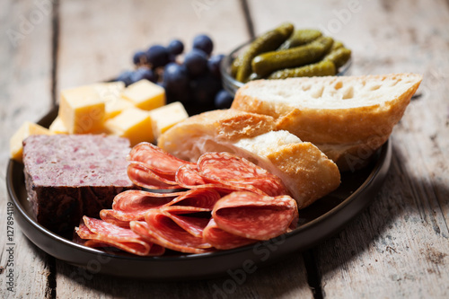 Charcuterie assortment, olives and gherkins  on plate on wooden background