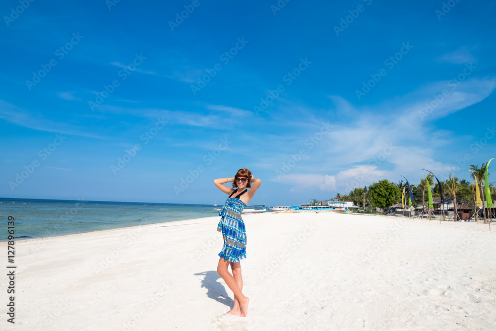 Happy sexy young woman in blue dress and sunglasses posing on Indonesian beach. Indian ocean, Beautiful blissful woman in blue dress enjoying tropical beach and indonesian summer vacation. Enjoying