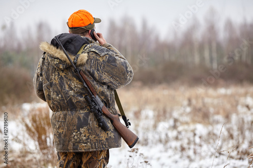 Hunter in camouflage clothes with hunting rifle and mobile phone during a winter hunting