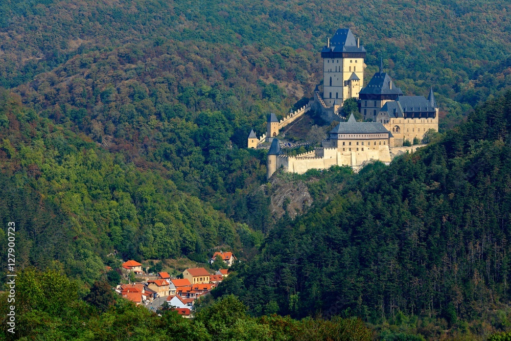 Obraz premium Gothic royal castle Karlstejn in green forest during autumn, Central Bohemia, Czech republic, Europe. State caste in with village in valley. Castle with tower in landscpae. Czech monument near Prague.