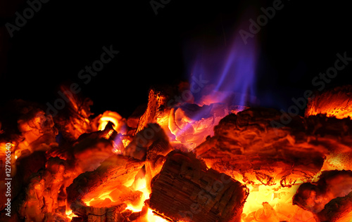 Beautiful fire in the fireplace or campfire with hot coals close-up macro. Languages spurts of blue flame on embers.