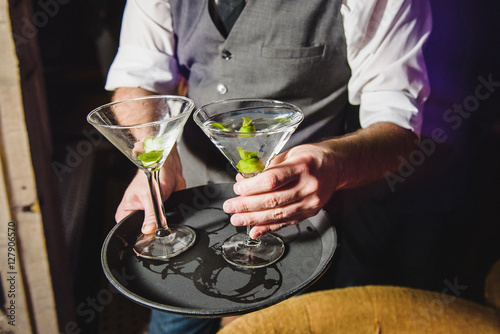 Waiter in grey waistcoat puts cocktail on the tray
