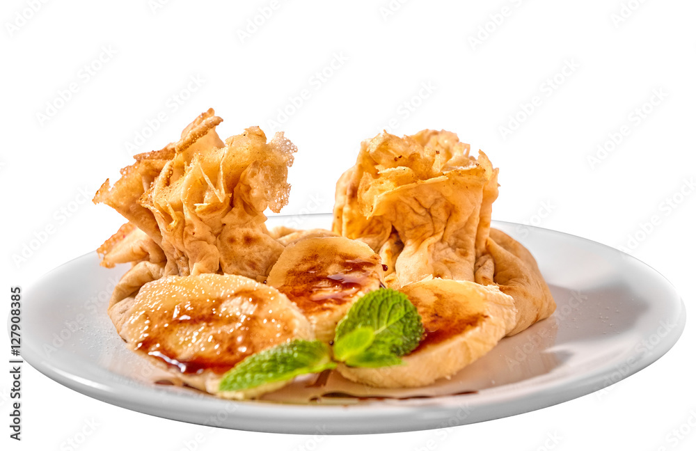 Traditional Romanian crepes with banana slices, hazelnut spread with cocoa and mint leaves decoration, on white plate and isolated on white background