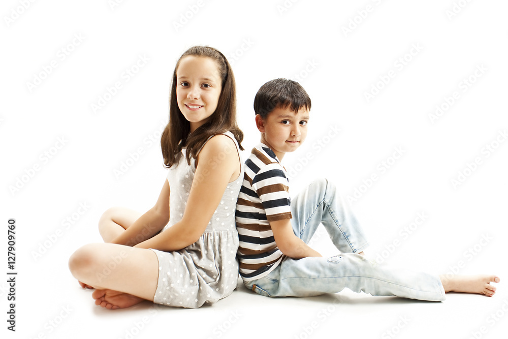 Happy young brother and sister posing back to back sitting on floor. Isolated on white backgroun Happy young brother and sister posing back to back sitting on floor. Isolated on white backgroun