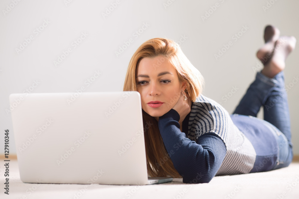 Beautiful adult woman lying on floor at home and using laptop Beautiful adult woman lying on floor at home and using laptop