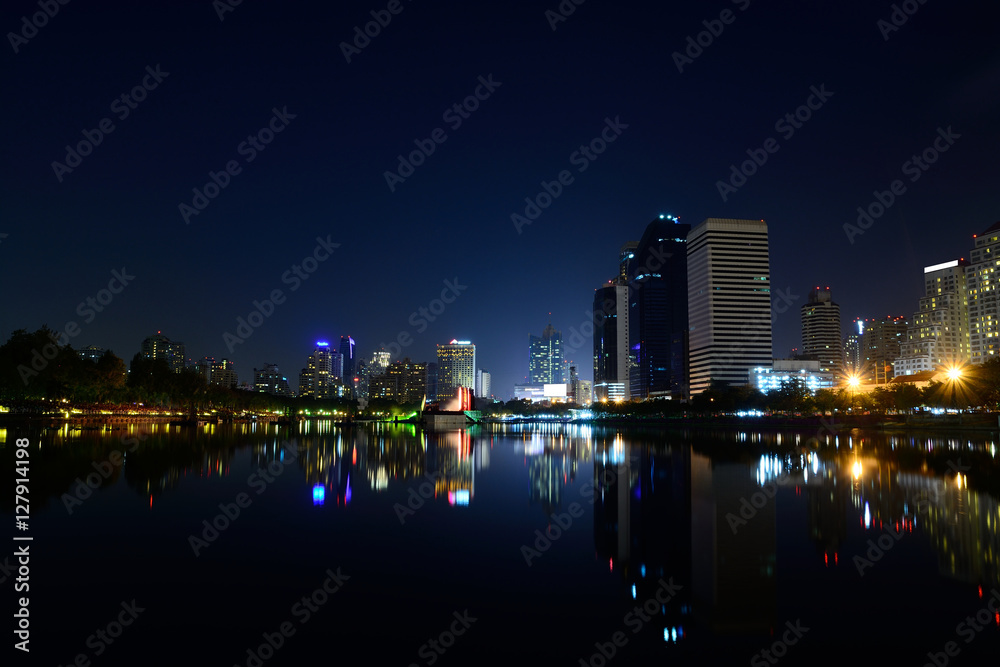 Obraz premium Modern city view of Bangkok, Thailand. Cityscape with Commercial Building Beside Lake in Public Park with Reflection at Twilight or Night