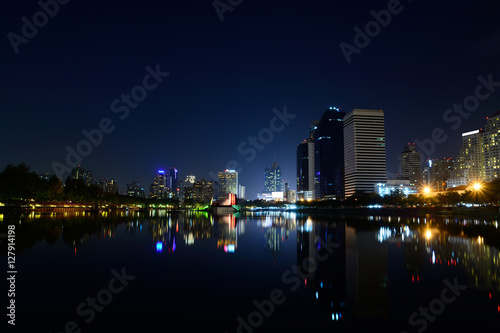 Modern city view of Bangkok, Thailand. Cityscape with Commercial Building Beside Lake in Public Park with Reflection at Twilight or Night