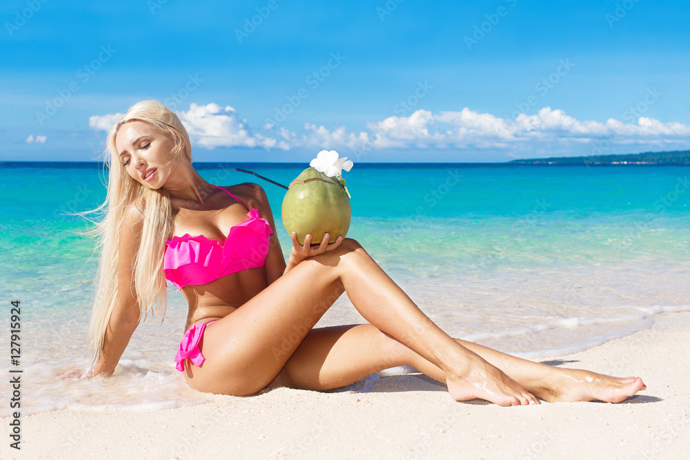 Beautiful blonde with long hair in bikini with coconut on a tropical beach. Blue sea in the background. Summer vacation concept. Beautiful blonde with long hair in bikini with coconut on a tropical beach. Blue sea in the background. Summer vacation concept.