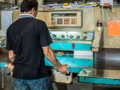 Asian man uesing paper cutter to make books.