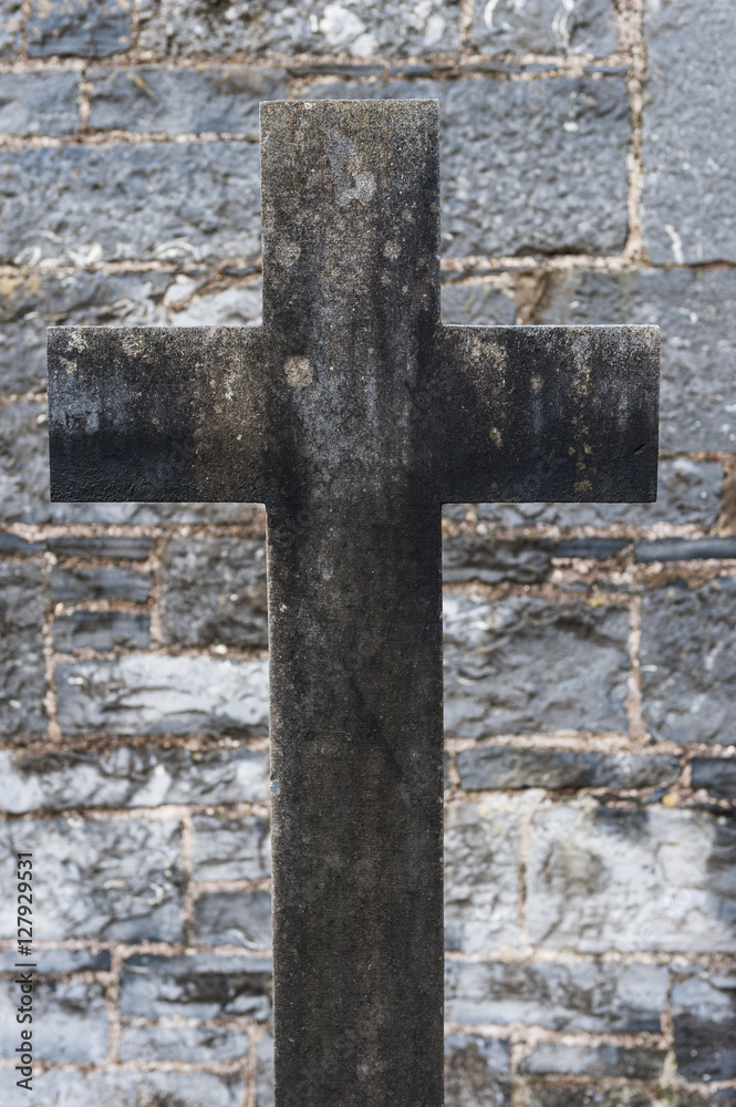 old grey concrete christian gravestone cross in front of stone wall background