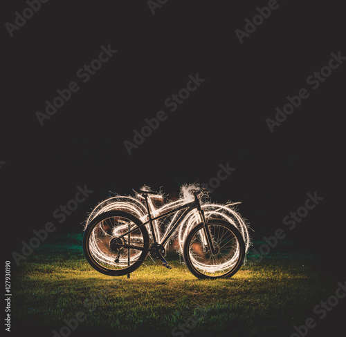 Silhouette of mountain bicycle on Green meadow with Beautiful Fireworks sparkler at night