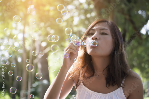 Beautiful woman wearing white dress blowing bubbles in the park,vintage style.