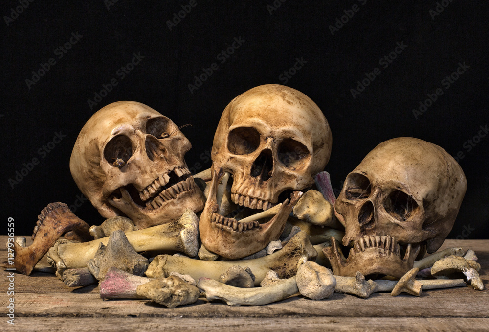 Obraz premium Three skull and pile of bone on old wooden plate