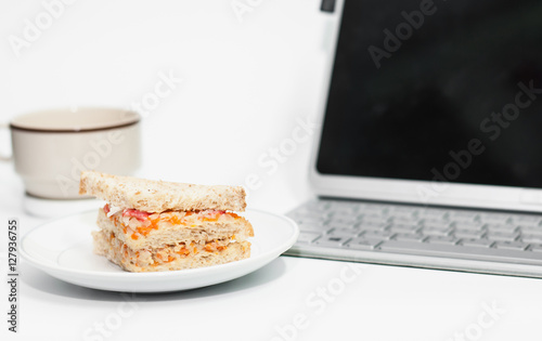 Sandwich on dish put on white table,laptop and coffee cup on tab