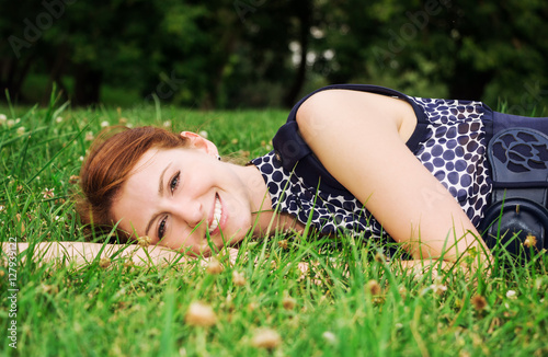 Beautiful young woman lying on green grass outdoor.