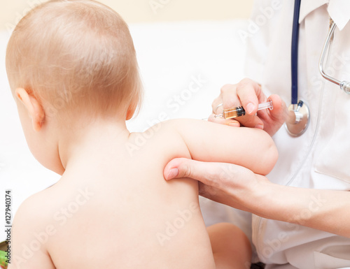 Close-up shot of pediatrician ready to give an intramuscular injection of a vaccine to a baby girl photo