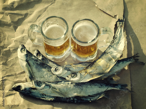 Two glasses of beer, salty fish and bones of dominoes on crumpled gray paper. Beer and snack to beer. photo