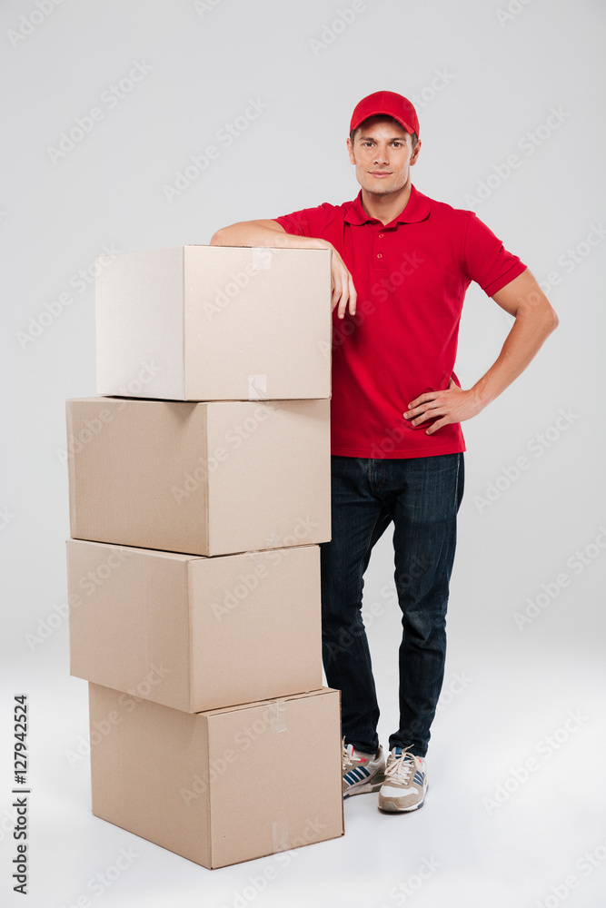 Smiling courier in red shirt leaning on stack of box
