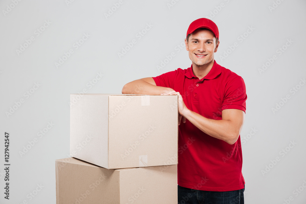 Happy smiling delivery man in red cap standing near boxes
