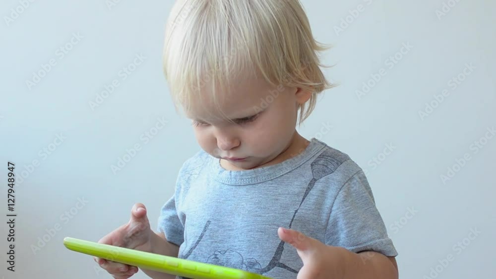 Little Girl Plays on the Tablet PC. Sometime She Raises Her Head and Looks to Camera. Little Girl Plays on the Tablet PC. Sometime She Raises Her Head and Looks to Camera.