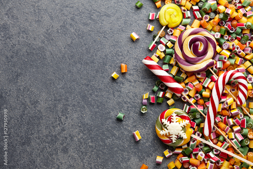 Colorful lollipops, candy canes and sweet candies mix on dark stone background