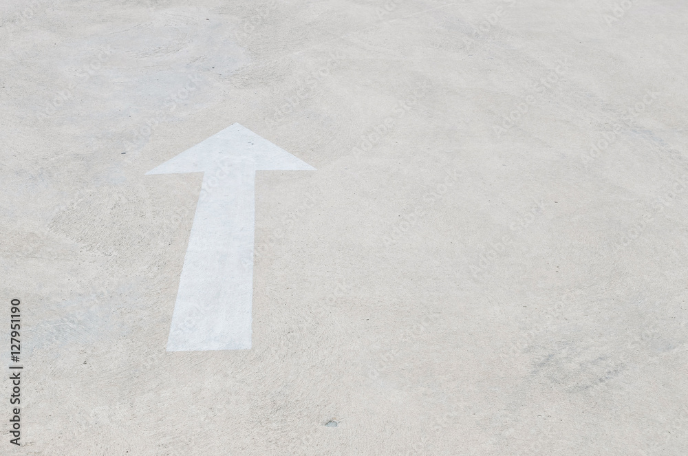 Closeup white painted arrow sign on cement street floor textured background with copy space Closeup white painted arrow sign on cement street floor textured background with copy space