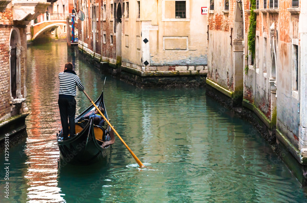 Through the canals of Venice. A Venetian gondolier propels a gondola.