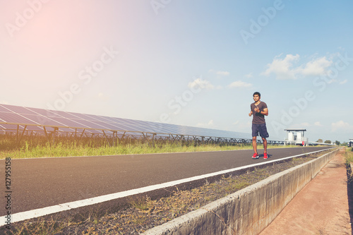 handsome man running on road with solar power plant in morning ;
