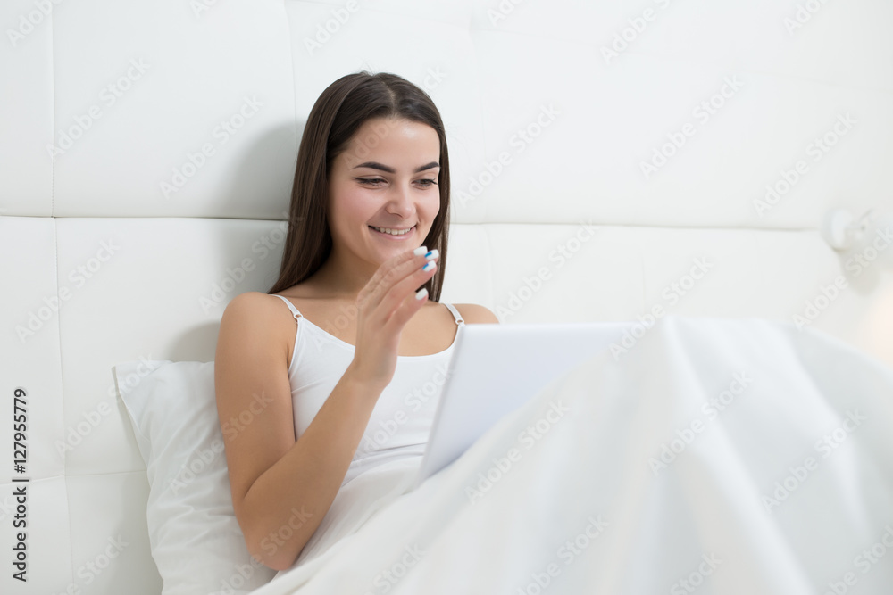 Woman using tablet at the morning. She lies on white bed Woman using tablet at the morning. She lies on white bed